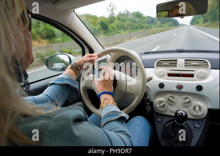 BOTTROP, Deutschland - 16.August 2018: Eine blonde Frau ist whatsapping auf Ihrem Smartphone, während Sie auf einer Autobahn in voller Geschwindigkeit fährt. Stockfoto