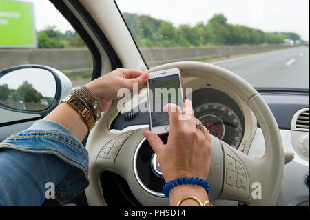 BOTTROP, Deutschland - 16.August 2018: Eine blonde Frau ist whatsapping auf Ihrem Smartphone, während Sie auf einer Autobahn in voller Geschwindigkeit fährt. Stockfoto