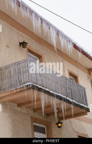 Große Eiszapfen hängen idyllisch aus mehreren Etagen eines Hauses Stockfoto