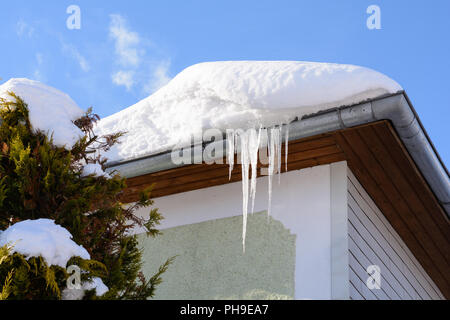 Schnee und Eiszapfen hängen vom Dach eines Hauses Stockfoto