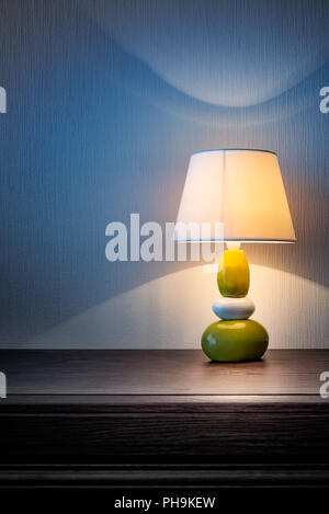 Kleine gelbe, graue und grüne Lampe auf Holz Kommode oder ein Nachttisch, beleuchten die Wand mit Tapeten in der Nacht oder am späten Abend abgedeckt. Weich Stockfoto