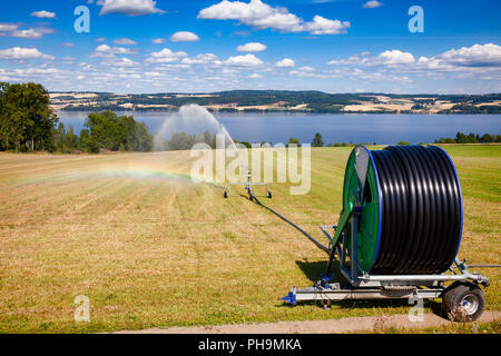 Reisen Sprinkler mit Schlauchhaspel Bewässerung Maschine spaying Wasser über einem Ackerland während einer Dürre im Sommer Stockfoto