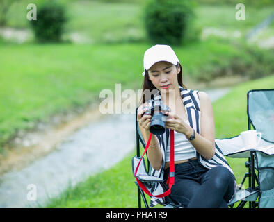 Asiatische Mädchen sitzt in der Nähe von Bach und Kontrolle Foto auf Kamera Stockfoto
