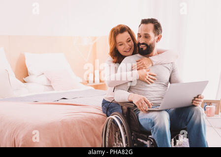Positive Frau ihren behinderten Mann umarmt Stockfoto