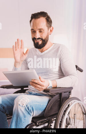 Fröhliche wheelchaired Mann mit Hilfe eines Tablet für die Kommunikation Stockfoto