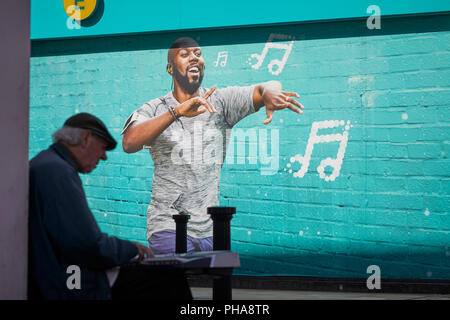 Ein strassenmusikant in Bolton, Lancashire führt neben und Werbung auf EE-Handy Shops Wand Stockfoto