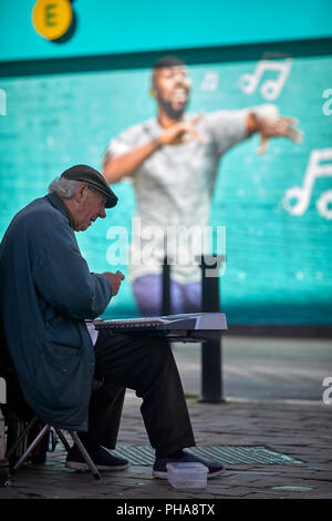 Ein strassenmusikant in Bolton, Lancashire führt neben und Werbung auf EE-Handy Shops Wand Stockfoto