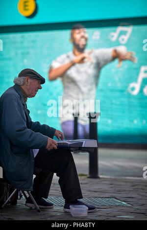 Ein strassenmusikant in Bolton, Lancashire führt neben und Werbung auf EE-Handy Shops Wand Stockfoto