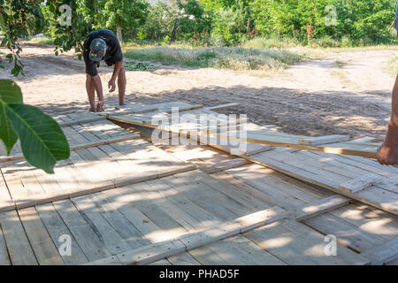 Menschen, der ein Holzzaun. Arbeitnehmer Abholung Holzplatten für den Zaun Schalung. Holz- schalungen für Beton auf der Baustelle. Stockfoto