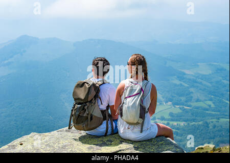 Junge Touristen Paar mit backpaks sitzen auf einer Flanke eines Berges genießen eine wunderschöne Aussicht. Stockfoto