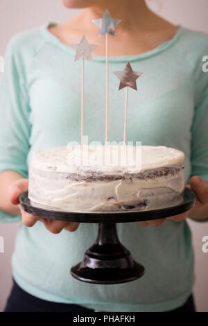 Woman's Hände, die köstlichen hausgemachten Kuchen Geburtstag weiß mit Sternen verziert. Hellblau hinterlegt. Backen zu Hause für Veranstaltungen. Kochen süße Cak Stockfoto