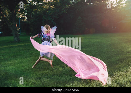 Portrait von laufenden blonde weiße Kaukasier Kind Mädchen mit langem Haar zu tragen rosa Fee Flügel und tutu Tüllrock große Stück Stoff, Stockfoto