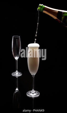 Eine Flasche Champagner in Strömen in zwei Sektkelche auf schwarzem Hintergrund Stockfoto
