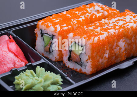 Satz von California Rolls in einem schwarzen 'take away'-Container auf einem schwarzen Hintergrund Seitenansicht Stockfoto