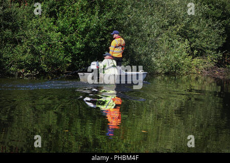 2 Mitarbeiter vom Kanal und Fluss das Vertrauen in die offiziellen Boot sprühen Chemikalien auf Unkräuter für eine riverbank Clean-up am Rande eines Flusses. Stockfoto