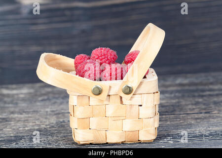 Beeren der roten Himbeeren in eine raue Holz- korb Liegen, Stehen auf einem Holztisch, Stockfoto