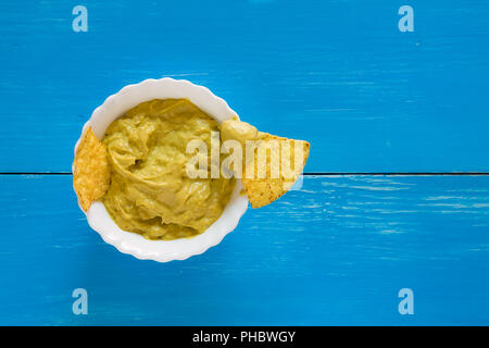 Nachos chips Eintauchen in Salsa Guacamole über einen blauen Hintergrund Stockfoto