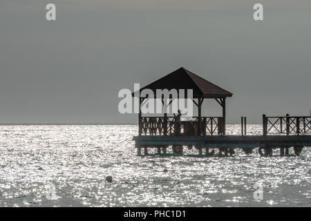 Bayahibe, Dominikanische Republik, 27. August 2018. Eine touristische verwendet Ihr Telefon an einer Pier über das Karibische Meer. Die grauen Look ist aufgrund der extremen Hintergrundbeleuchtung Stockfoto
