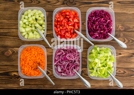 Kunststoffbehälter mit verschiedenen bunten Frisch geschnittenes Gemüse für einen Salat oder als einzelne Beilagen in den ordentlichen Reihen angeordnet auf einem Holztisch vie Stockfoto