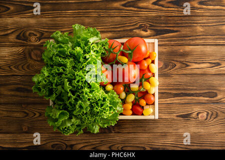 Frischen Kopf von Grünem Salat und eine Vielzahl von Reifen saftigen Tomaten in einer kleinen Holzkiste an den hölzernen Tisch in einem organischen Farmers Market am Holzkasten Stockfoto