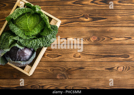 Zwei frische Köpfe von Savoyen und Rotkohl nebeneinander in einer Holzkiste, die auf einem Tisch an den hölzernen Tisch in einem organischen Farmers Market gesehen von oben mit c Stockfoto