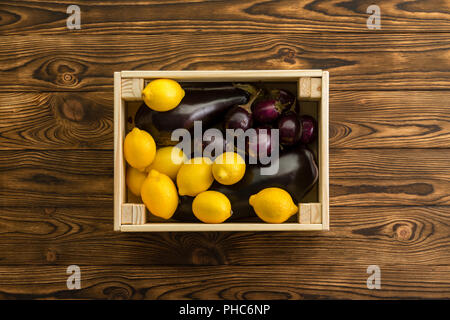 Farbenfrohe gelbe Zitronen und violetten Aubergine zusammen in einer kleinen Holzkiste Holztisch auf eine organische Farmers Market von oben Zentrum gesehen verpackt Stockfoto