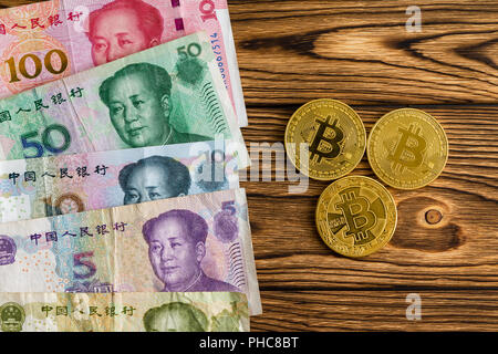Sortierte Chinese Yuan arrangiert als Grenze neben drei Bitcoins auf einem hölzernen Tisch in einem Vergleich zwischen einer nationalen Währung und virtuelle digitale Stockfoto