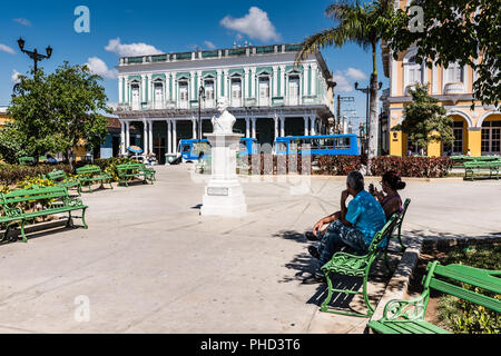 Sancti Spiritus, Kuba/15. März 2017: Traditionelle spanische Park mit grünen Bänken und weißen Stein Denkmal. Stockfoto