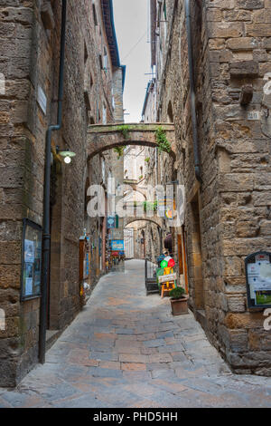 VOLTERA ITALIEN - 21. APRIL 2011; schmale Gasse durch hohe Gebäude aus Stein mit Small Business und Cafés Stockfoto