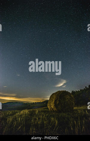 Wunderschöne Aussicht auf starred Nacht Himmel mit Wolken über ein bebautes Feld mit Heu Ballen Stockfoto