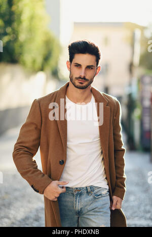 Junger Mann mit Winterkleidung in der Straße. Junge Bartgeier Kerl mit modernen Frisur mit Mantel, blaue Jeans und weißen T-Shirt. Stockfoto