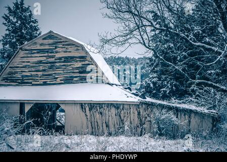 Frischer Schnee sitzt auf dem Boden um eine alte Scheune Stockfoto