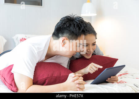 Paare mit Tablet auf dem Bett liegend Stockfoto