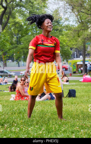 Junge und charmante Afro-amerikanische Frauen mit einer roten und gelben Jersey shorts Tanz auf den Gräsern des Mount Royal Park in Montreal, Quebec, Kanada. Stockfoto