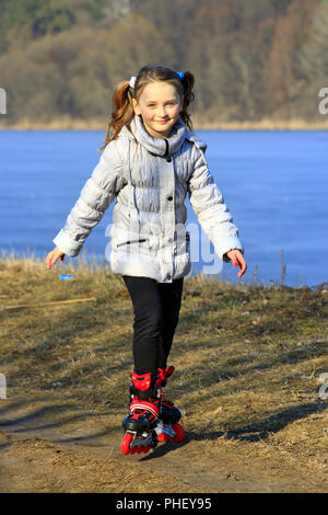 junges schönes Mädchen geht in Inline Skates auf dem Boden Stockfoto