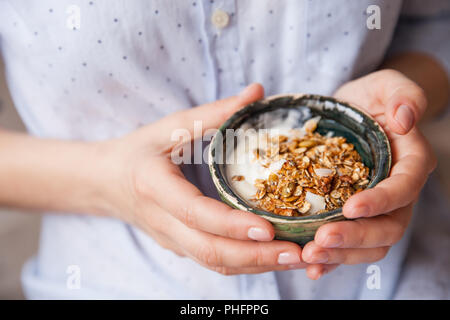 Junge Frau mit Müsli Schüssel. Frühstück Müsli mit Nüssen, Kürbiskerne, Hafer und Joghurt in der Schüssel. Hände, die hausgemachtes Müsli. Gesunden Snack. Stockfoto