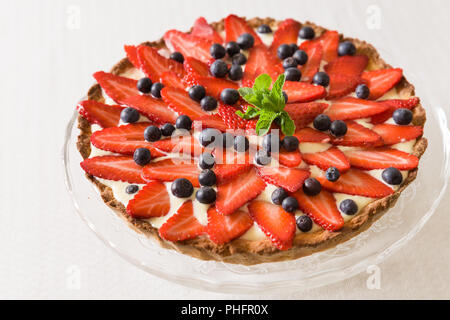 Hausgemachter Käsekuchen mit Erdbeeren, Heidelbeeren und frische Minze- und Cremetönen eingerichtet. Schöne Torte für einen Urlaub oder einen Geburtstag Feiern teil Stockfoto