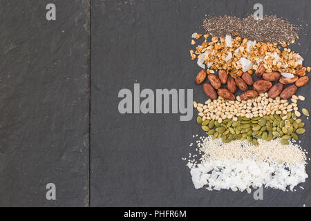 Bunt gestreiften Reihen mit Kokosraspeln, Sesam, Kürbiskerne, Kakaobohnen, Müsli und Chia Samen. Mischung der unterschiedlichen Art der bunte Bohnen Stockfoto