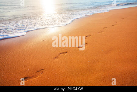Strand, Wellen und Fußabdrücke bei Sonnenuntergang Stockfoto