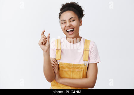 Ha-ha so klein. Portrait von freudiger gefühlvolle junge Frau mit dunkler Haut und lockige Haare, Gestaltung kleine und lustige Objekt mit den Fingern, vor Lachen, laut, Schelte jemand Ursache der Grösse über graue Wand Stockfoto