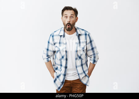 Guy Gefühl überrascht, Geld in der Tasche von alten Hose. Portrait von überrascht und begeistert auf der Suche Mann mit Bart, falten Lippen beim Sagen wow, von der Kamera begeistert anstarren, posierend über graue Wand Stockfoto