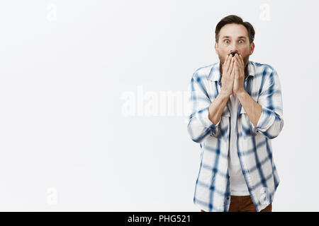 Portrait von entsetzt, fassungslos und emotional reifer Mann mit Bart in kariertes Hemd, der Mund mit Palmen und Starrte mit Augen geknallt bei Kamera, wird überrascht und von schrecklichen Nachrichten erstaunt Stockfoto