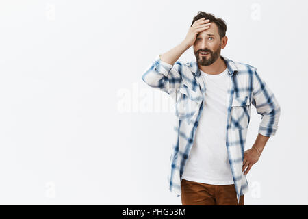 Frau betrunken, Mann in Verlegenheit gebracht wird, kann sich bei Frau, gedemütigt, Palm Holding an der Stirn und starrte mit Missfallen Ausdruck, berühren, Taille, stehend über grauer Hintergrund Stockfoto