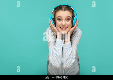 Happy girl in gestreiften blaues Hemd und pigtail Frisur, Musik hören und Ihre Kopfhörer Holding und Kamera mit toothy Lächeln, ICH Stockfoto