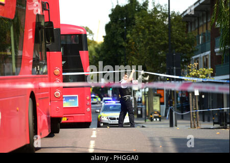 Ein Polizeioffizier cordons off der Bereich auf dem Caledonian Road in Islington, nördlich von London, wo ein Mann nach einer jungen Frau verhaftet wurde, war während einer Tageslicht Angriff niedergestochen. Stockfoto