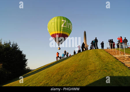 Strathaven Hot Air Balloon Festival 2018 - Kleine Stadt Unterhaltung, bunte Luftballons, Leute auf einem Hügel beobachten die Ballons steigen nach oben, und entfernen Sie sie Stockfoto