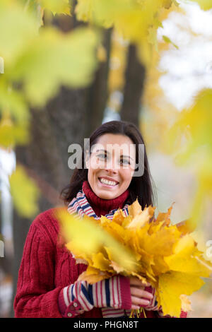 Junge lächelnde Frau mit bunten Ahornblätter in einem Herbst Park Stockfoto