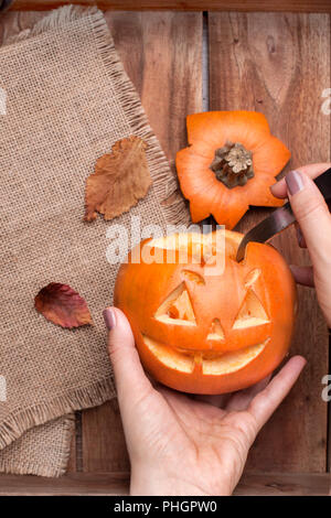 Kürbis für Halloween in Frauenhand, die Vorbereitung auf die Herbstferien. Blätter und Einrichtung auf einem Holztisch. Ansicht von oben. Stockfoto