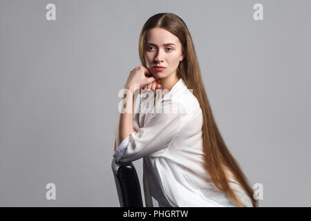 Portrait von verwirrt Traurigkeit nachdenkliche junge Modell Schauspieler mit langen braunen Haaren im weißen T-Shirt sitzen auf schwarzen Stuhl und Wegsehen und dissatisfi Stockfoto