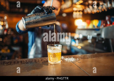 Männliche Barkeeper Schürze gießt aus einem Getränk durch ein Sieb in ein Glas. Der Barkeeper an der Theke. Alkohol Getränke Vorbereitung Stockfoto